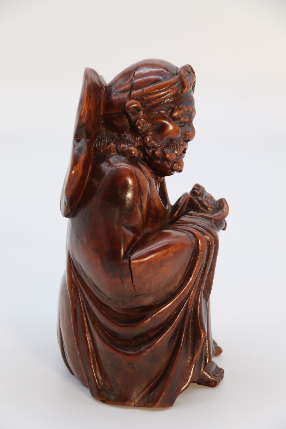 A fine Japanese carved hardwood mid 19th century Okimono of a seated man holding a bat. View IV