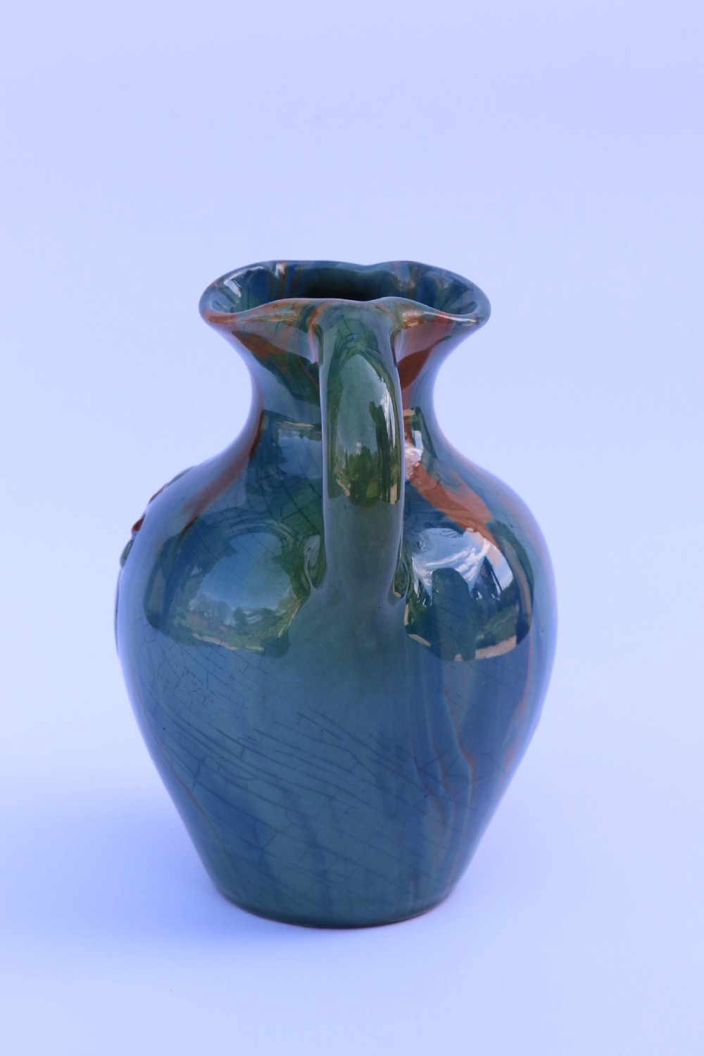 A teal blue Arts and Crafts earthenware studio pottery jug featuring raised floral slipwork motifs, red glazed highlights, and a pinched spout. View VIII