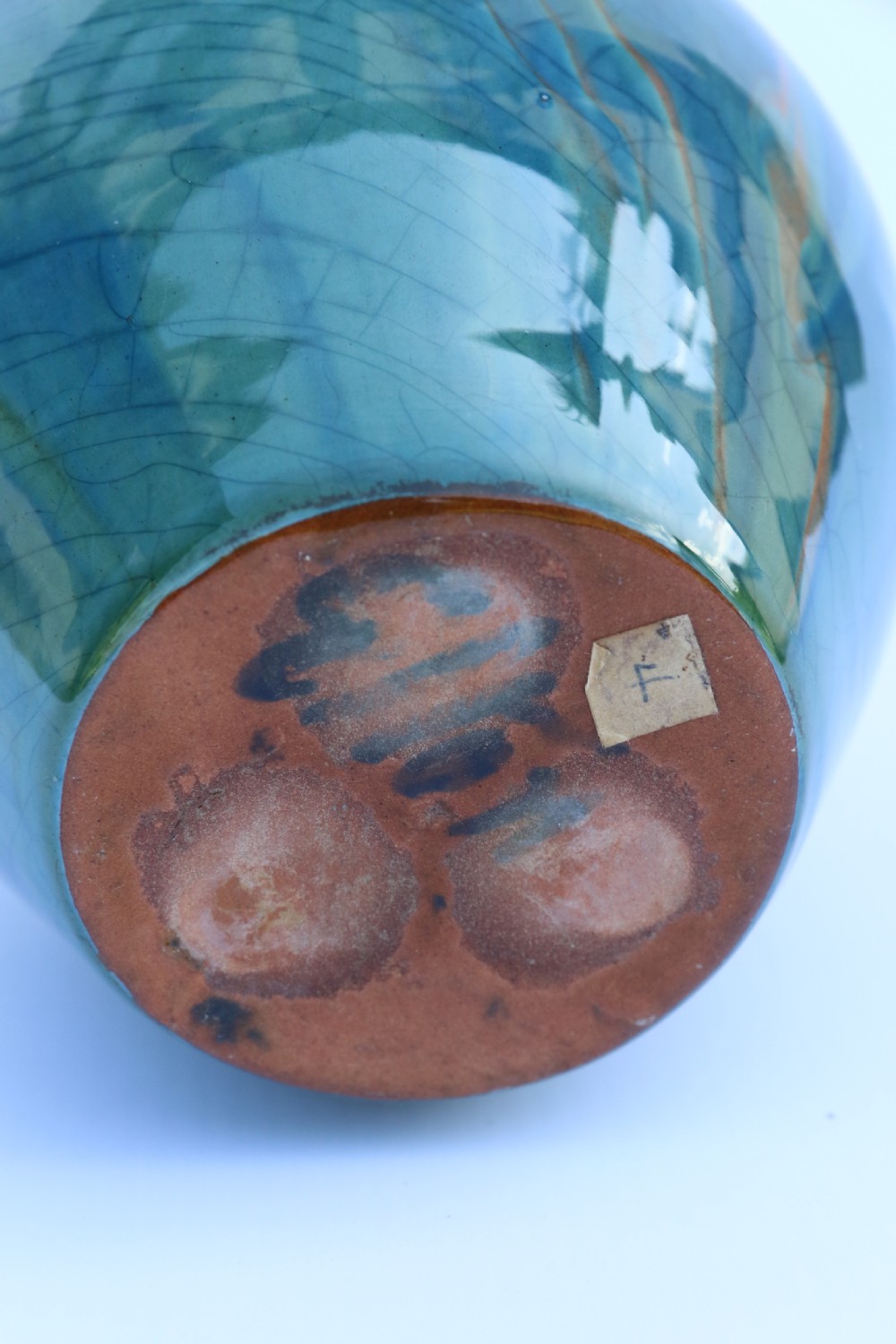 A teal blue Arts and Crafts earthenware studio pottery jug featuring raised floral slipwork motifs, red glazed highlights, and a pinched spout. View X