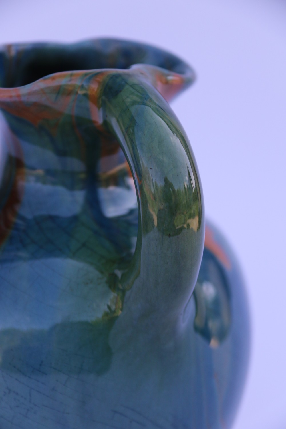 A teal blue Arts and Crafts earthenware studio pottery jug featuring raised floral slipwork motifs, red glazed highlights, and a pinched spout. View XVI