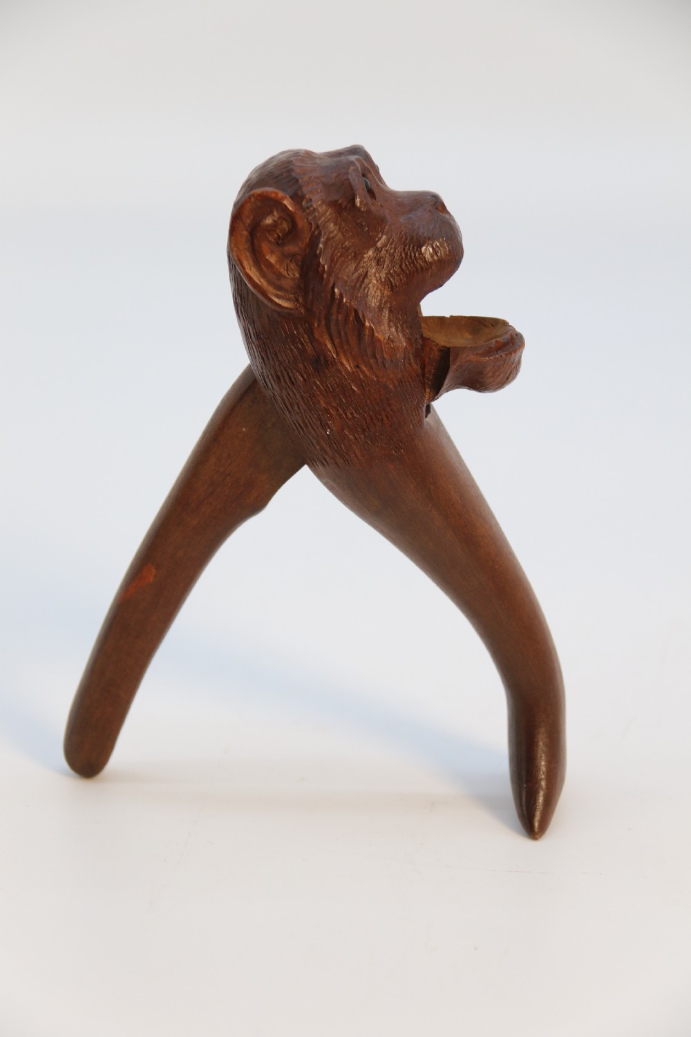 A hand-carved walnut nutcracker shaped as a monkey head with glass bead eyes and a hinged jaw mechanism. View II
