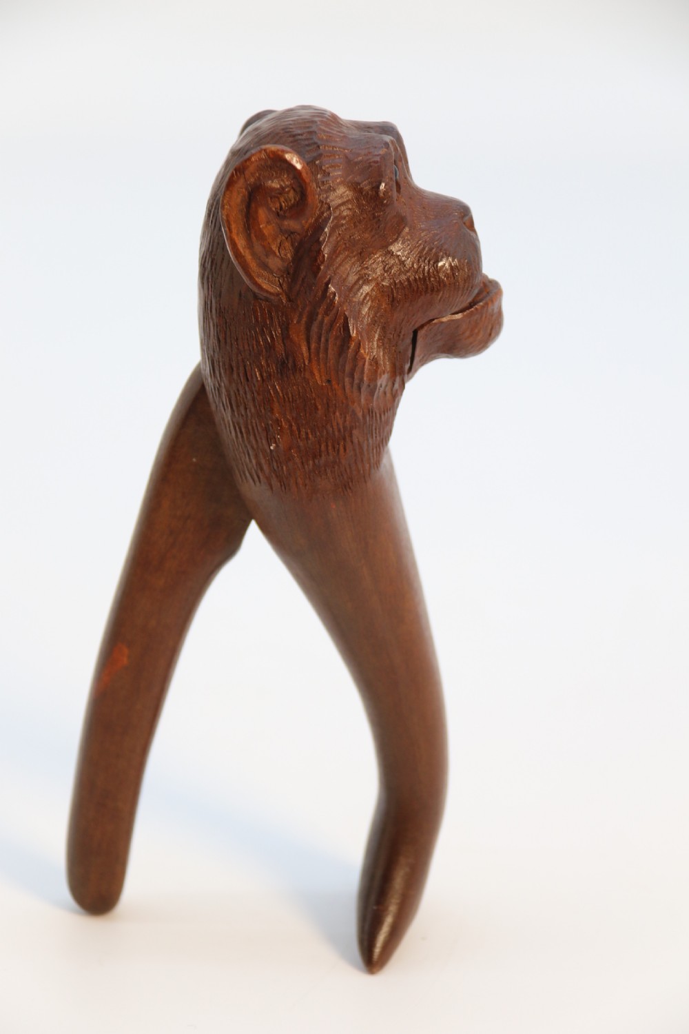 A hand-carved walnut nutcracker shaped as a monkey head with glass bead eyes and a hinged jaw mechanism. View X