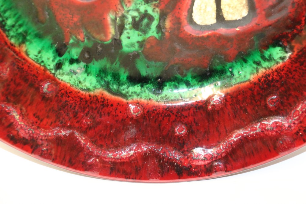 A circular glazed ceramic charger featuring a stylised cream horse motif against a deep red and emerald green reactive glaze. View V