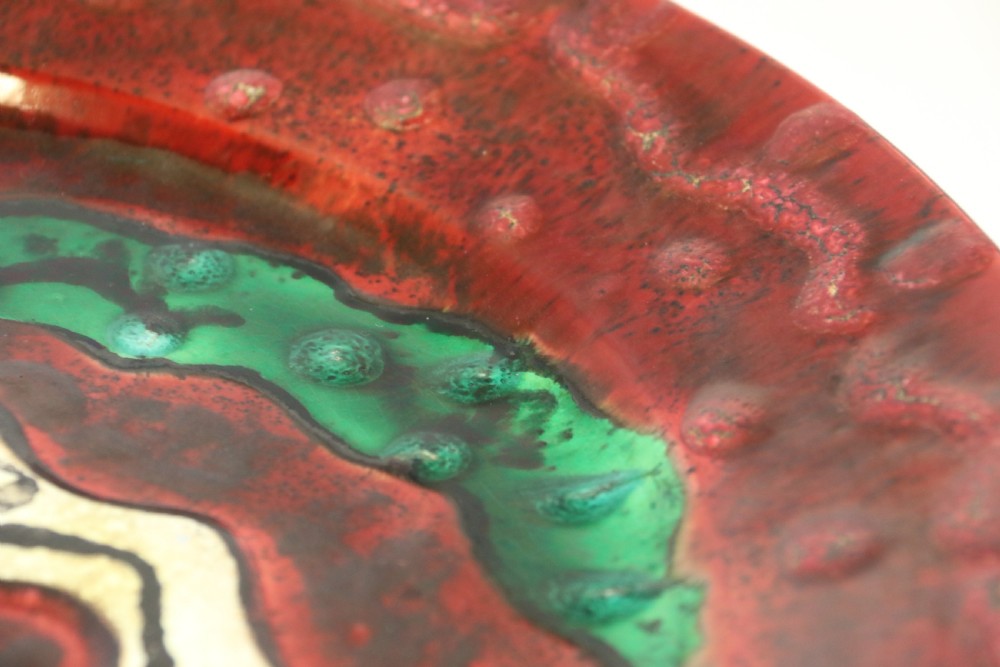 A circular glazed ceramic charger featuring a stylised cream horse motif against a deep red and emerald green reactive glaze. View XII