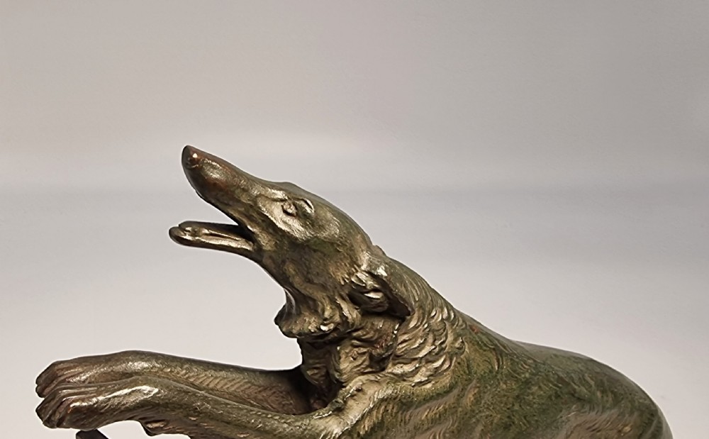 An Art Deco patinated bronze sculpture depicting a Russian borzoi hound leaping over a dark hurdle mounted on a two-tone marble base. View V