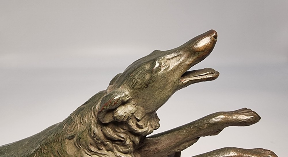 An Art Deco patinated bronze sculpture depicting a Russian borzoi hound leaping over a dark hurdle mounted on a two-tone marble base. View VII
