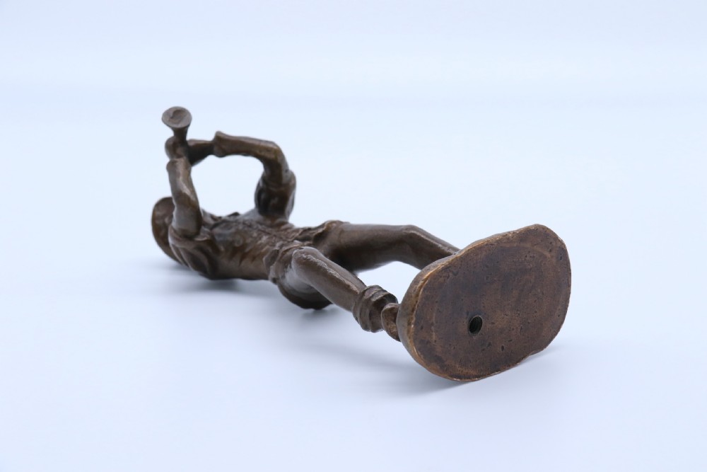 A dark brown patinated bronze statuette depicting a figure in historic costume playing a pipe while standing on a textured base. View XV