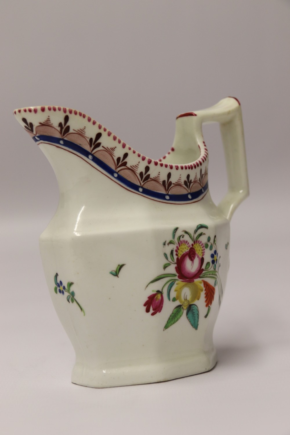 An 18th-century cream-coloured porcelain jug featuring hand-painted floral motifs, a decorated rim border, and an angular handle. View II