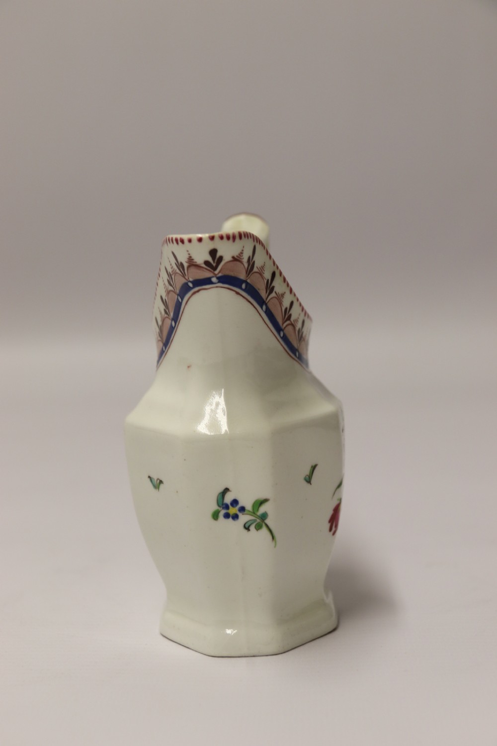 An 18th-century cream-coloured porcelain jug featuring hand-painted floral motifs, a decorated rim border, and an angular handle. View III