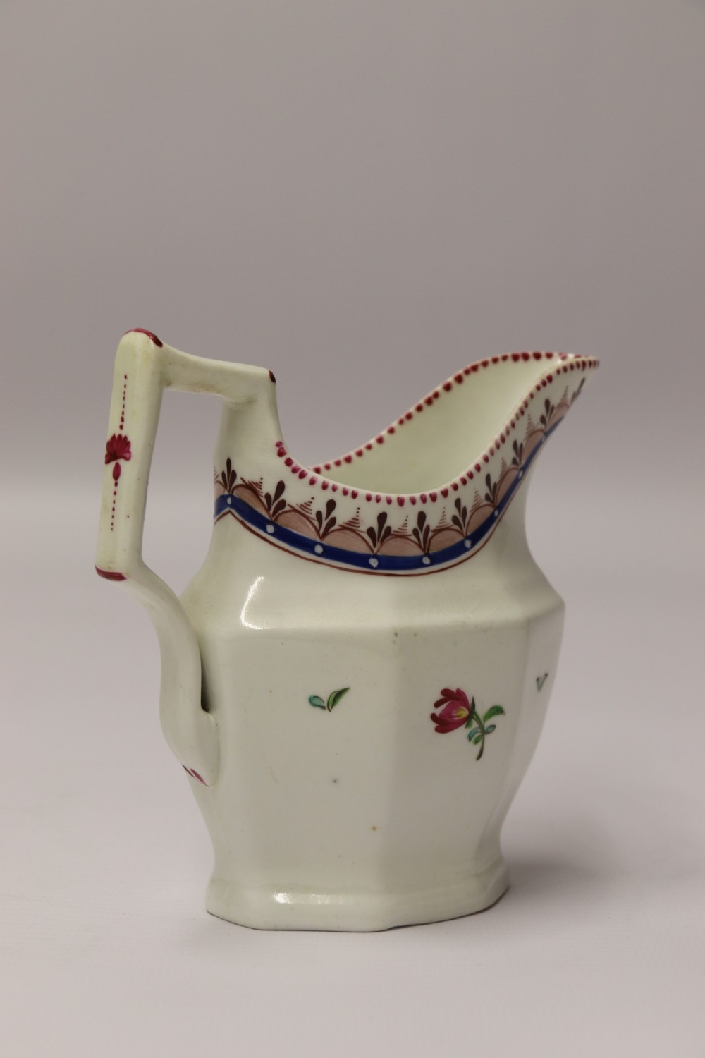 An 18th-century cream-coloured porcelain jug featuring hand-painted floral motifs, a decorated rim border, and an angular handle. View VII