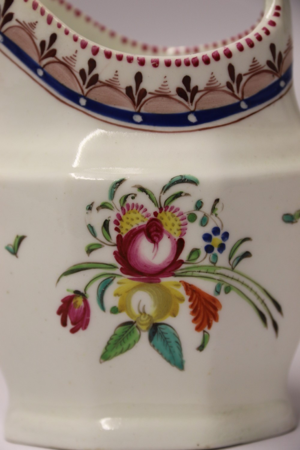 An 18th-century cream-coloured porcelain jug featuring hand-painted floral motifs, a decorated rim border, and an angular handle. View XI