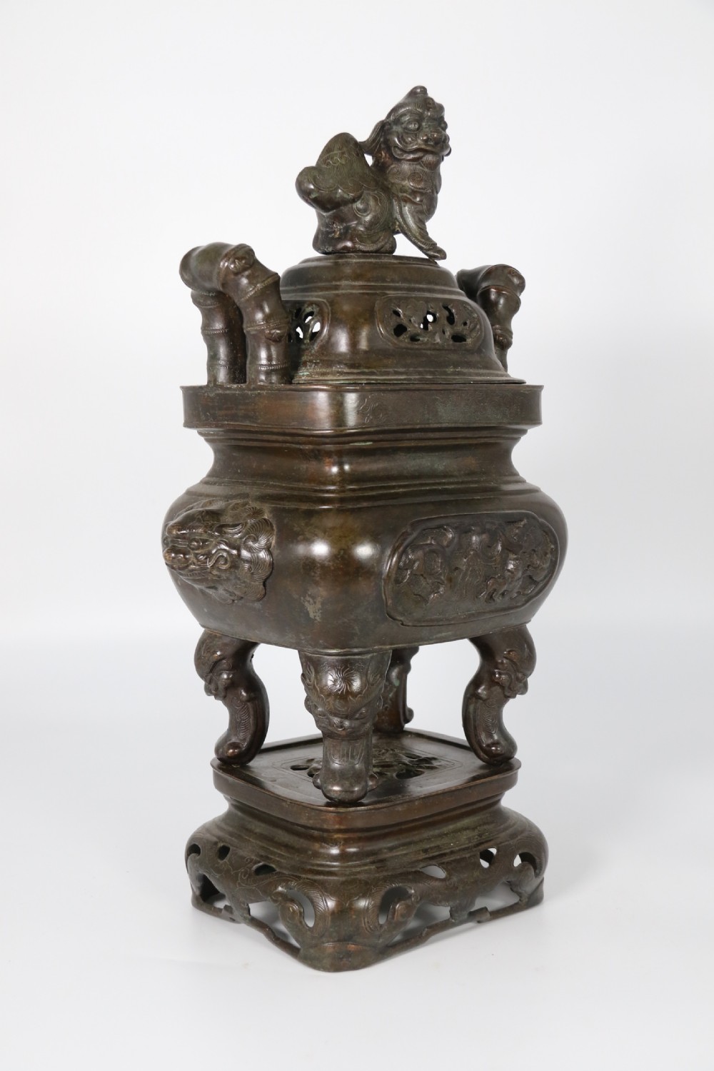 A 19th-century Chinese cast bronze incense censer featuring a lid surmounted by a guardian lion finial, relief panels, and animal-mask handles, set upon a matching bronze base. View II