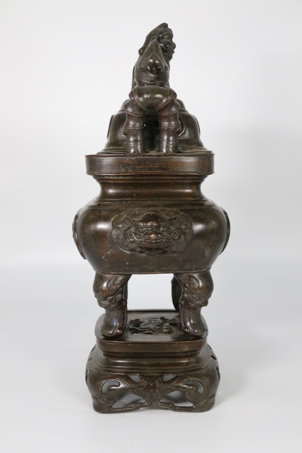 A 19th-century Chinese cast bronze incense censer featuring a lid surmounted by a guardian lion finial, relief panels, and animal-mask handles, set upon a matching bronze base. View III