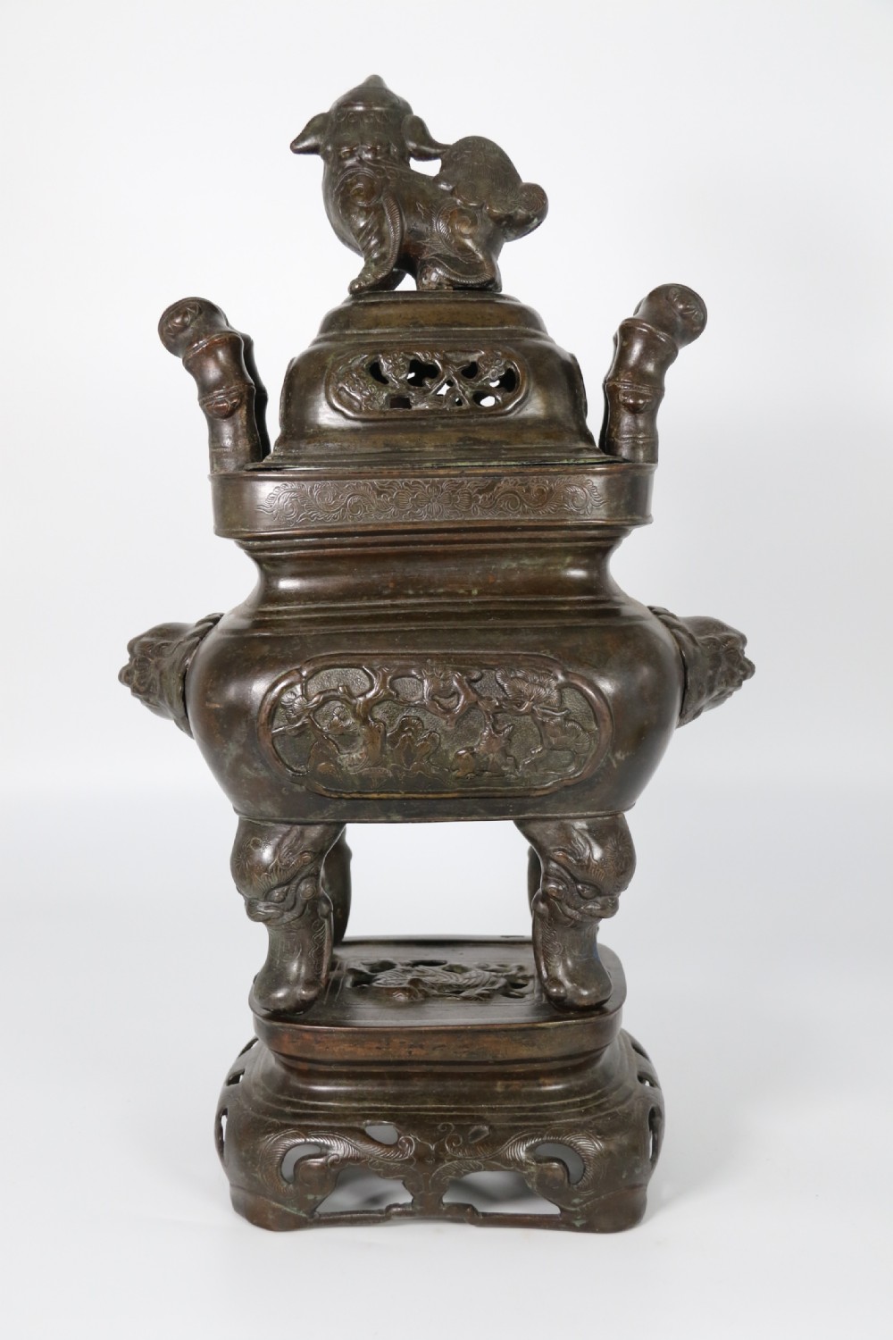 A 19th-century Chinese cast bronze incense censer featuring a lid surmounted by a guardian lion finial, relief panels, and animal-mask handles, set upon a matching bronze base. View VI