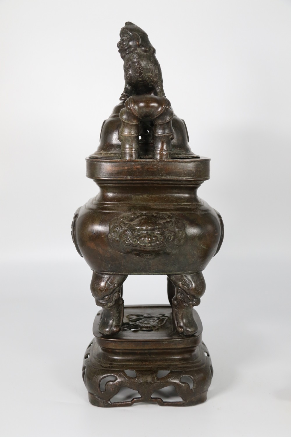 A 19th-century Chinese cast bronze incense censer featuring a lid surmounted by a guardian lion finial, relief panels, and animal-mask handles, set upon a matching bronze base. View VII