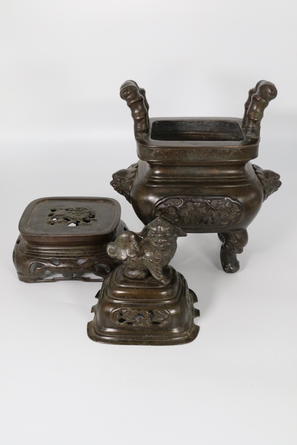 A 19th-century Chinese cast bronze incense censer featuring a lid surmounted by a guardian lion finial, relief panels, and animal-mask handles, set upon a matching bronze base. View IX