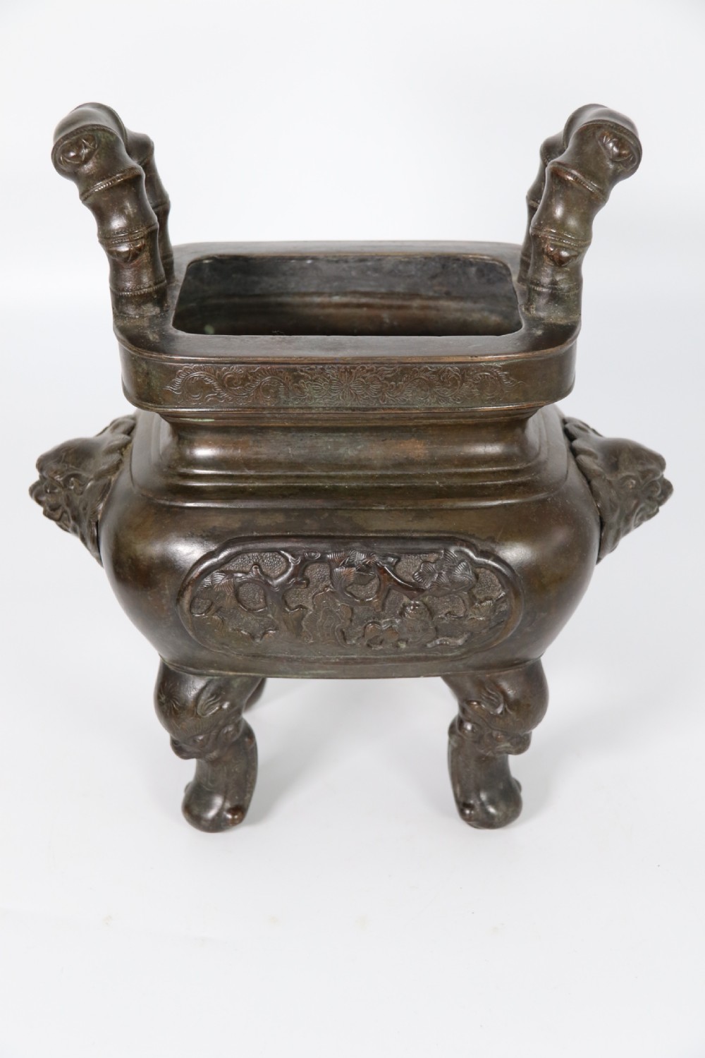 A 19th-century Chinese cast bronze incense censer featuring a lid surmounted by a guardian lion finial, relief panels, and animal-mask handles, set upon a matching bronze base. View X