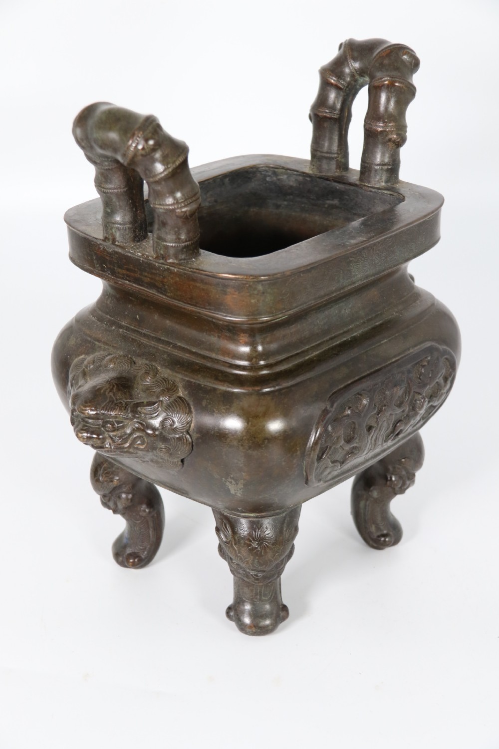 A 19th-century Chinese cast bronze incense censer featuring a lid surmounted by a guardian lion finial, relief panels, and animal-mask handles, set upon a matching bronze base. View XI