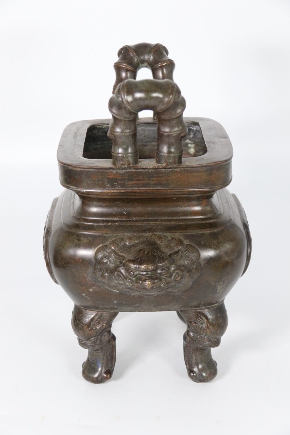 A 19th-century Chinese cast bronze incense censer featuring a lid surmounted by a guardian lion finial, relief panels, and animal-mask handles, set upon a matching bronze base. View XII