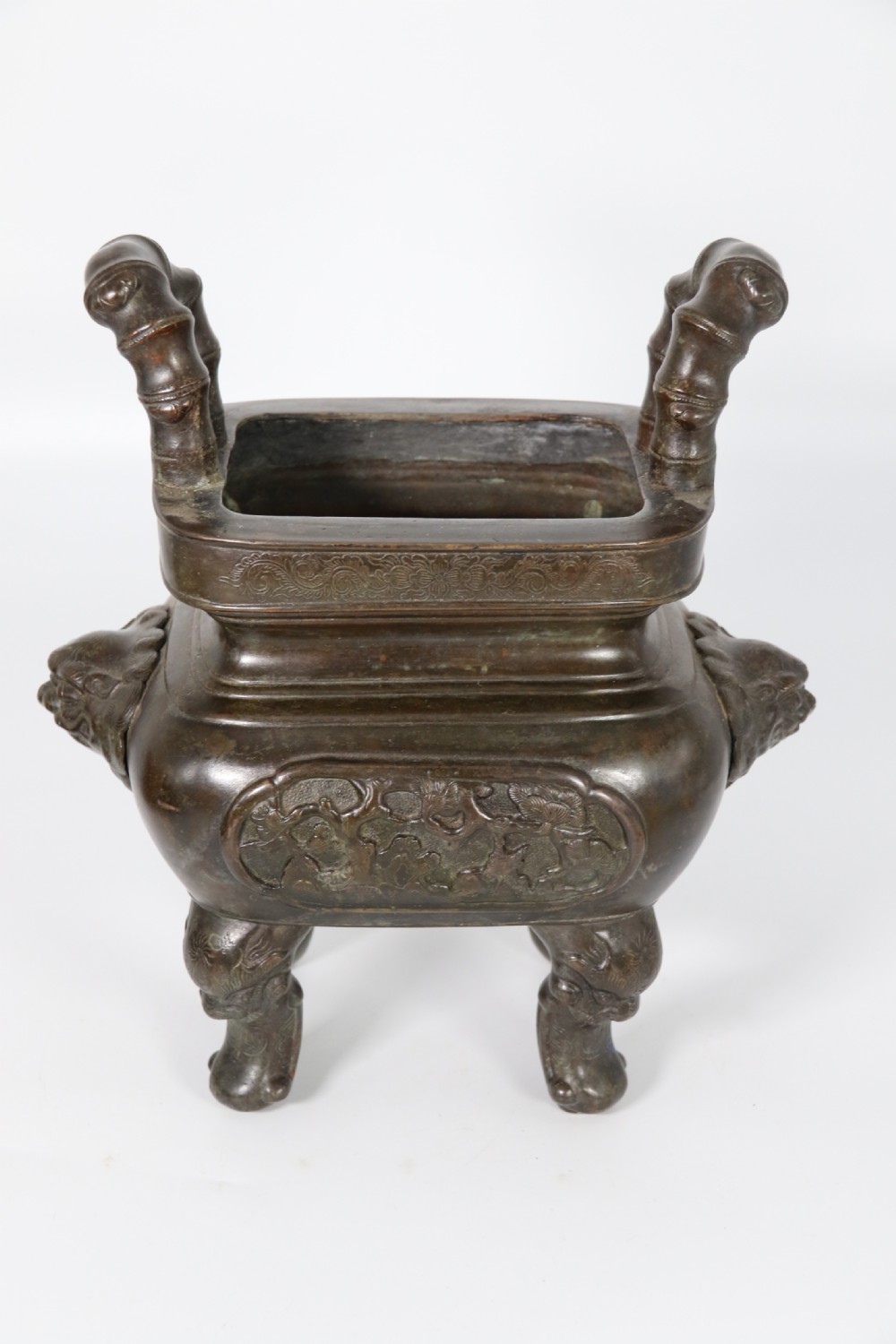 A 19th-century Chinese cast bronze incense censer featuring a lid surmounted by a guardian lion finial, relief panels, and animal-mask handles, set upon a matching bronze base. View XIV