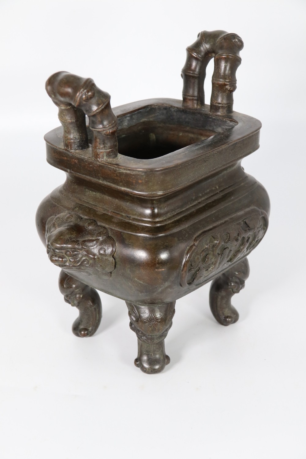 A 19th-century Chinese cast bronze incense censer featuring a lid surmounted by a guardian lion finial, relief panels, and animal-mask handles, set upon a matching bronze base. View XV