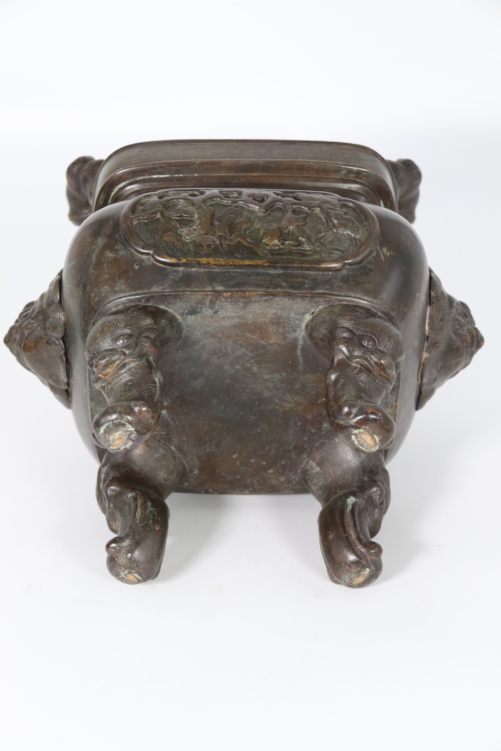 A 19th-century Chinese cast bronze incense censer featuring a lid surmounted by a guardian lion finial, relief panels, and animal-mask handles, set upon a matching bronze base. View XVI