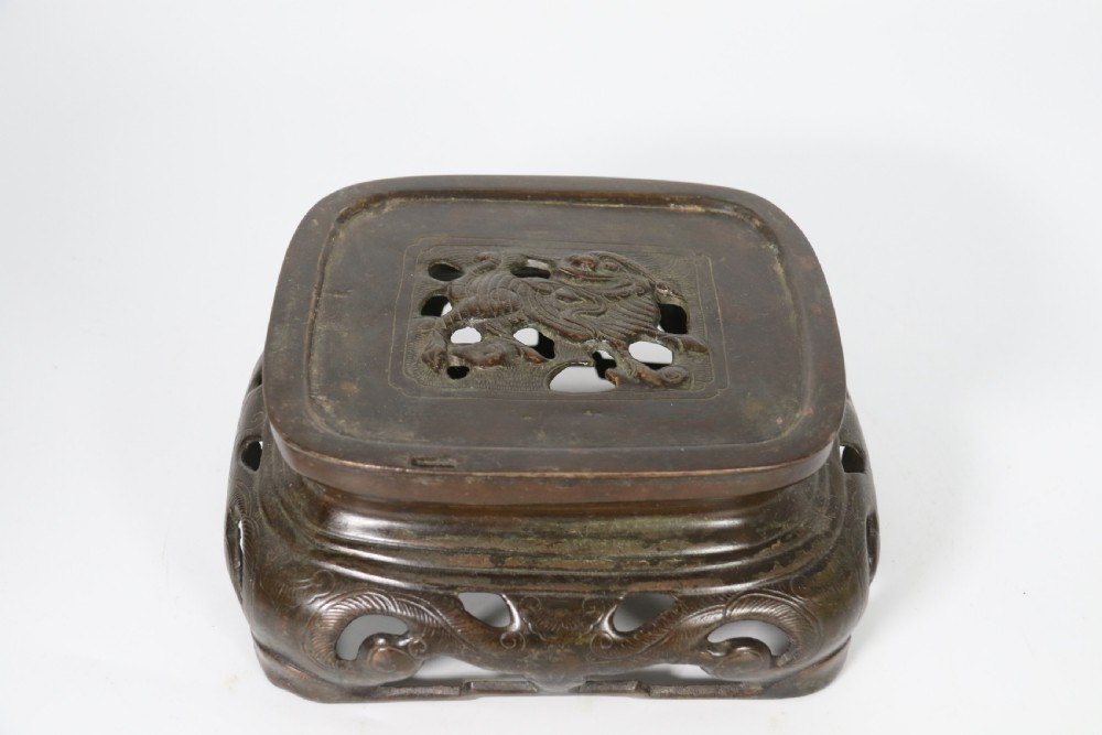 A 19th-century Chinese cast bronze incense censer featuring a lid surmounted by a guardian lion finial, relief panels, and animal-mask handles, set upon a matching bronze base. View XVII