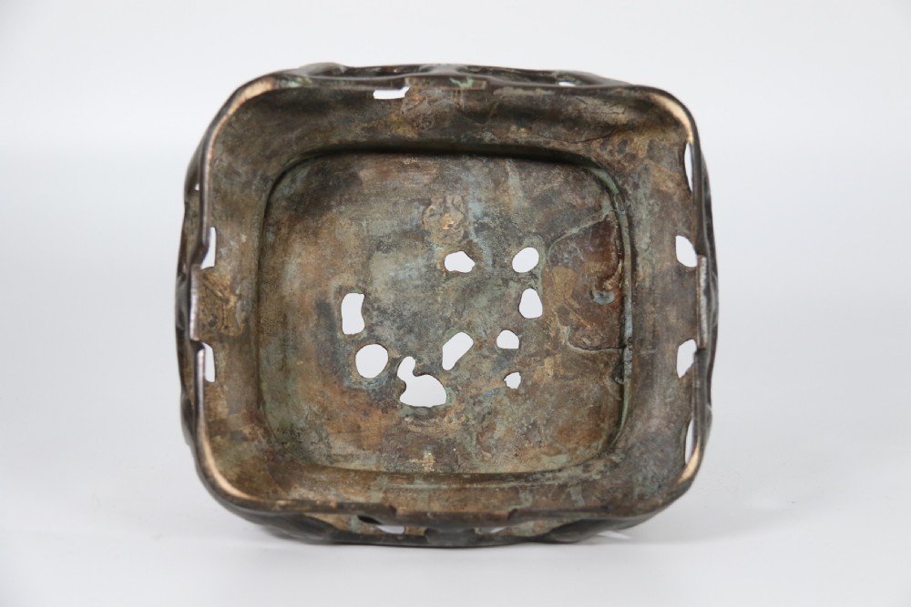 A 19th-century Chinese cast bronze incense censer featuring a lid surmounted by a guardian lion finial, relief panels, and animal-mask handles, set upon a matching bronze base. View XIX