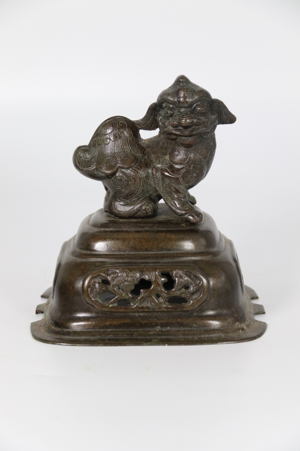A 19th-century Chinese cast bronze incense censer featuring a lid surmounted by a guardian lion finial, relief panels, and animal-mask handles, set upon a matching bronze base. View XX