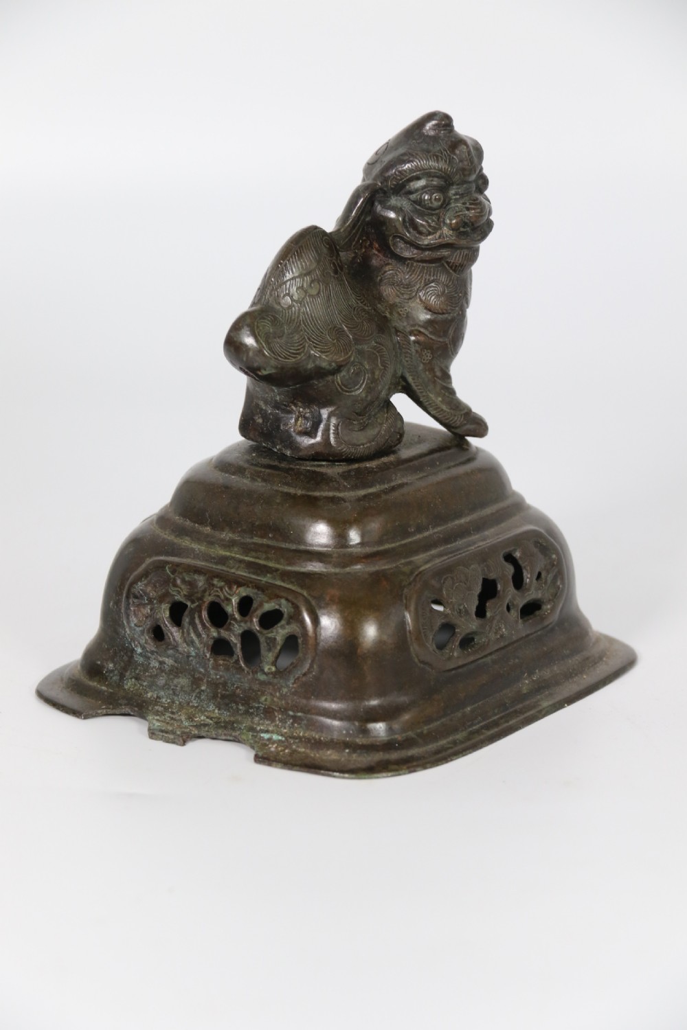 A 19th-century Chinese cast bronze incense censer featuring a lid surmounted by a guardian lion finial, relief panels, and animal-mask handles, set upon a matching bronze base. View XXI