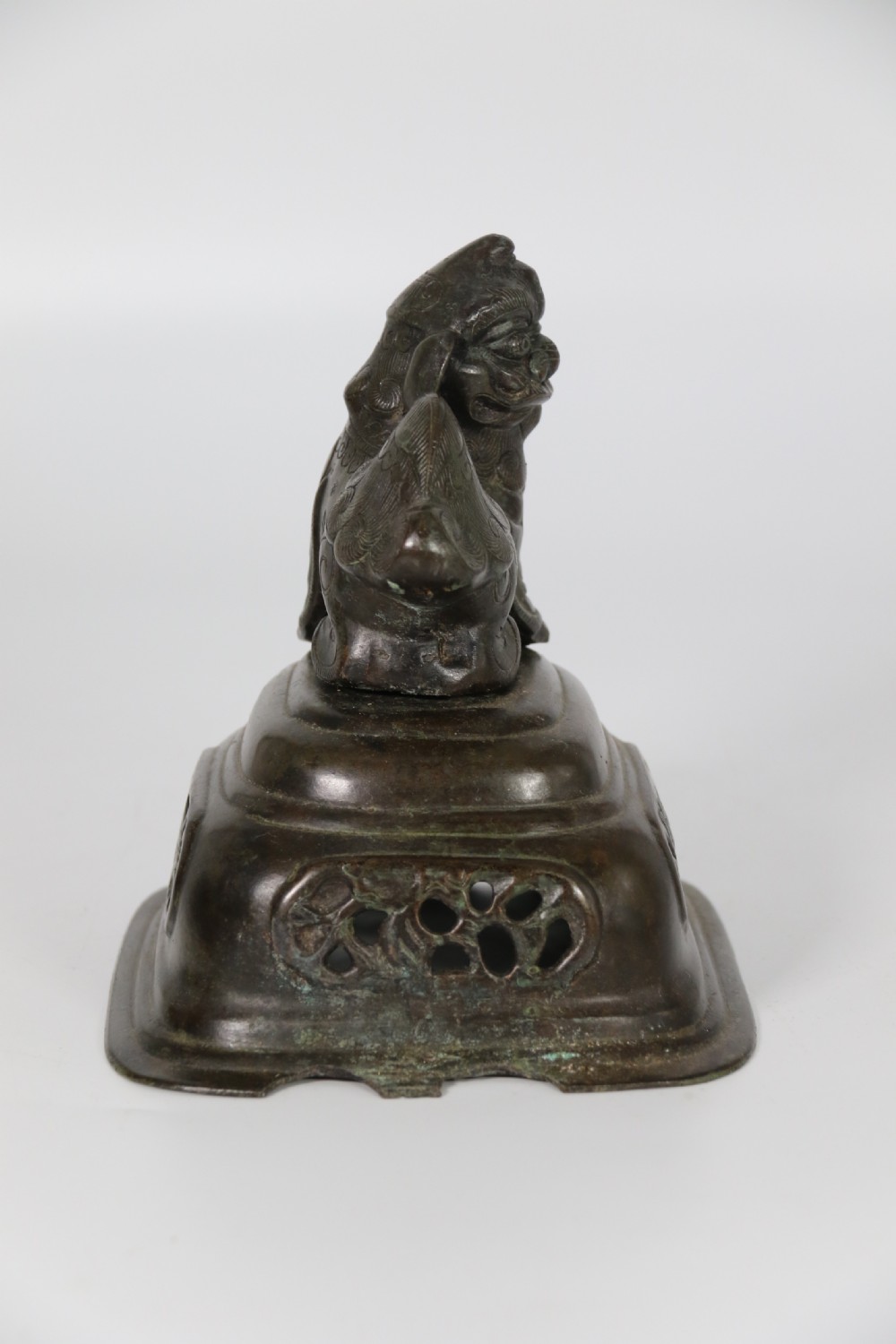 A 19th-century Chinese cast bronze incense censer featuring a lid surmounted by a guardian lion finial, relief panels, and animal-mask handles, set upon a matching bronze base. View XXII