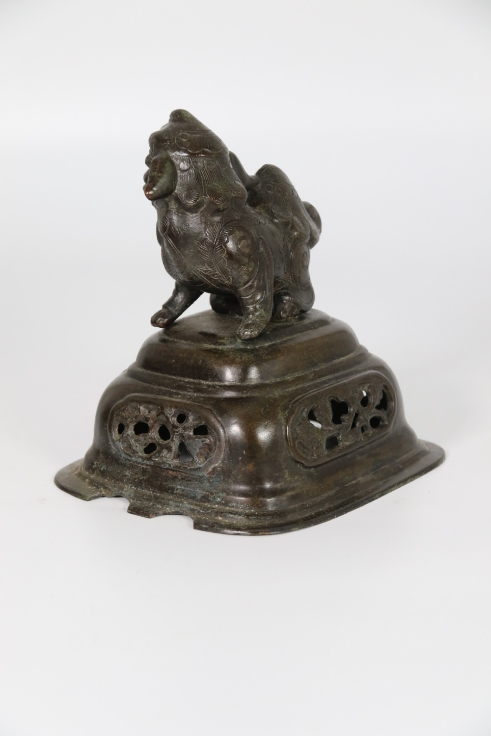 A 19th-century Chinese cast bronze incense censer featuring a lid surmounted by a guardian lion finial, relief panels, and animal-mask handles, set upon a matching bronze base. View XXIV