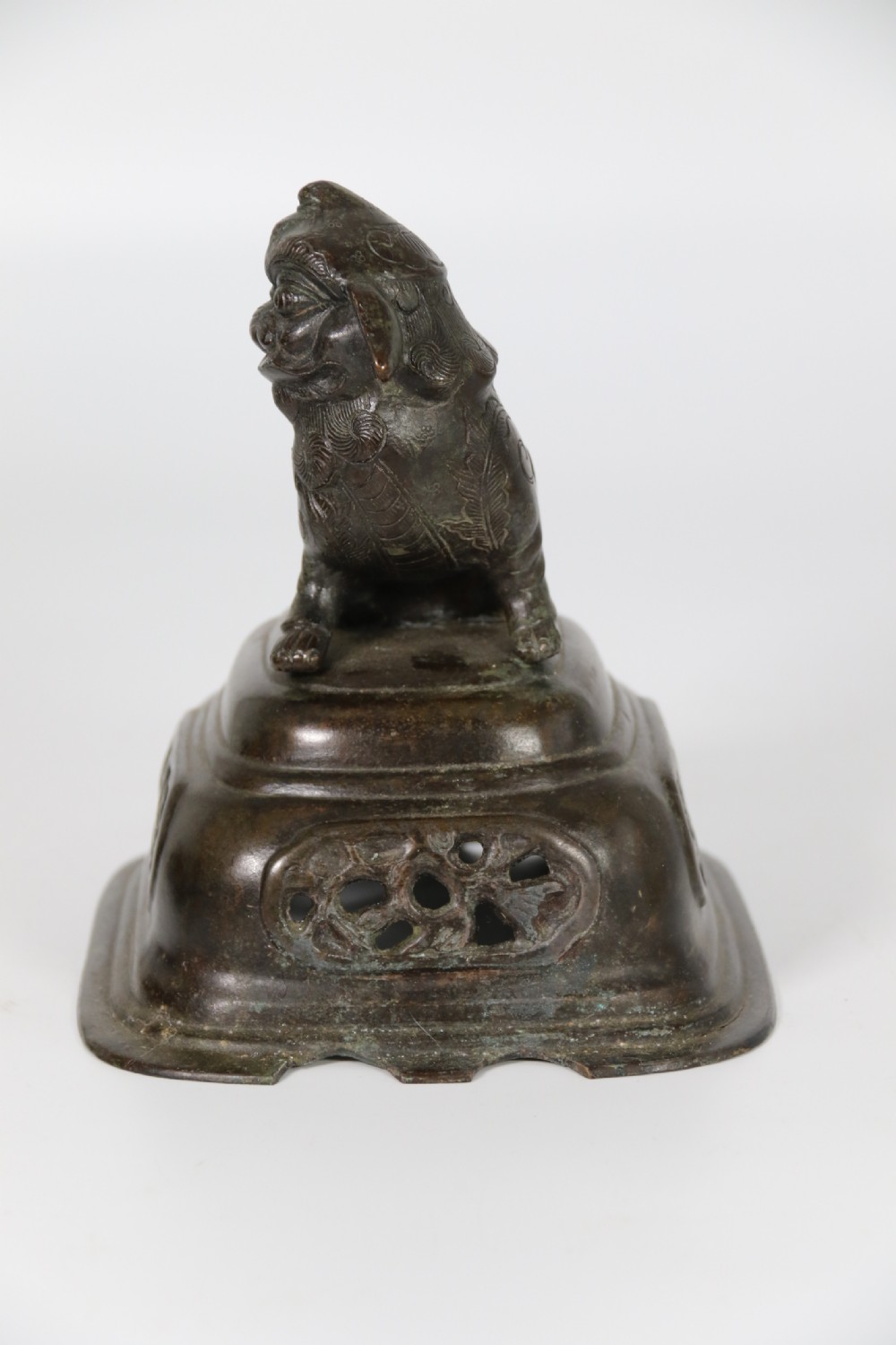 A 19th-century Chinese cast bronze incense censer featuring a lid surmounted by a guardian lion finial, relief panels, and animal-mask handles, set upon a matching bronze base. View XXV