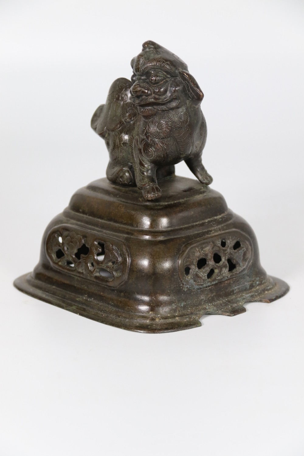 A 19th-century Chinese cast bronze incense censer featuring a lid surmounted by a guardian lion finial, relief panels, and animal-mask handles, set upon a matching bronze base. View XXVI