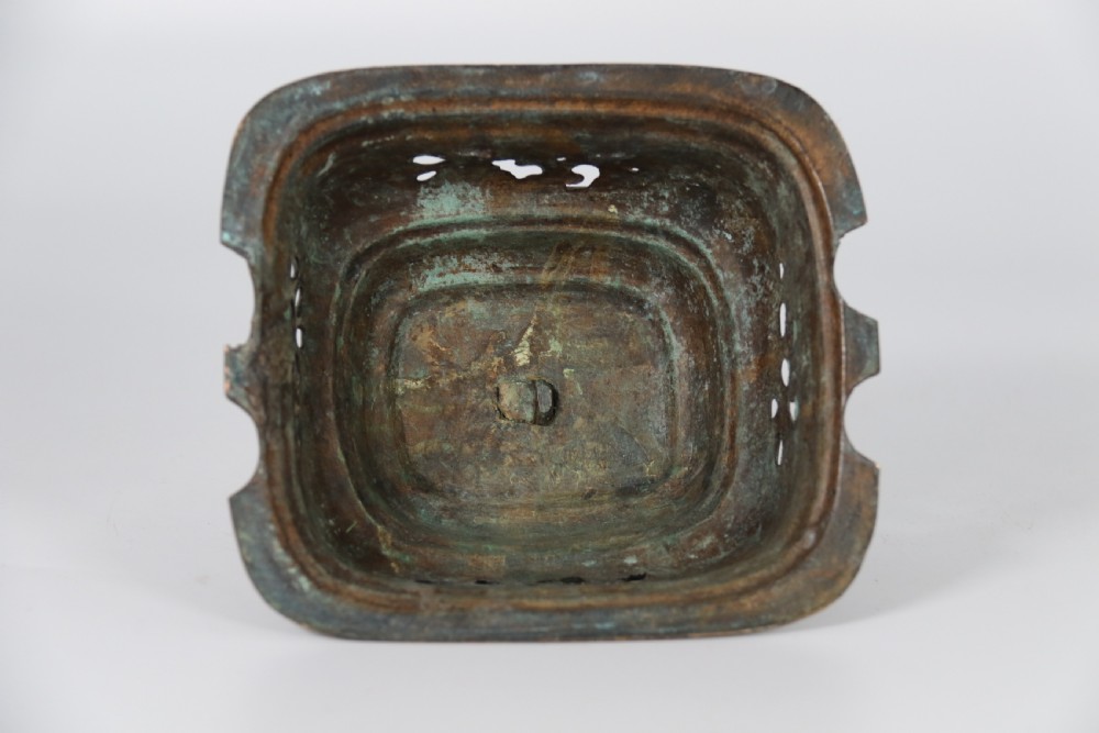 A 19th-century Chinese cast bronze incense censer featuring a lid surmounted by a guardian lion finial, relief panels, and animal-mask handles, set upon a matching bronze base. View XXVII