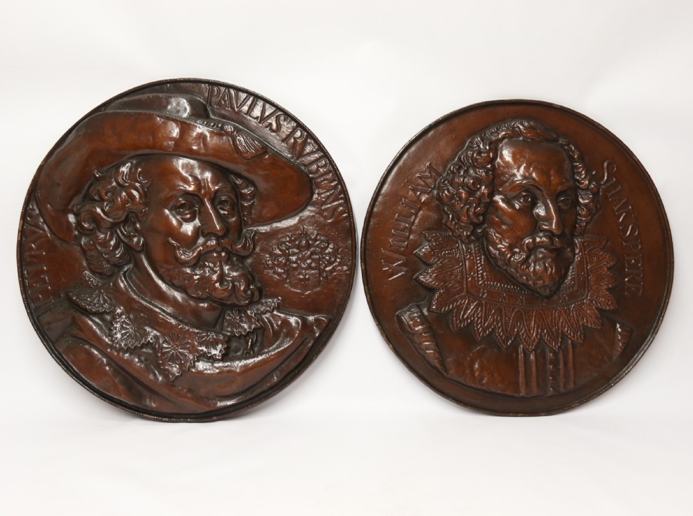 A matched pair of circular dark brown cast iron relief plaques featuring high-relief portrait busts of Peter Paul Rubens and William Shakespeare.