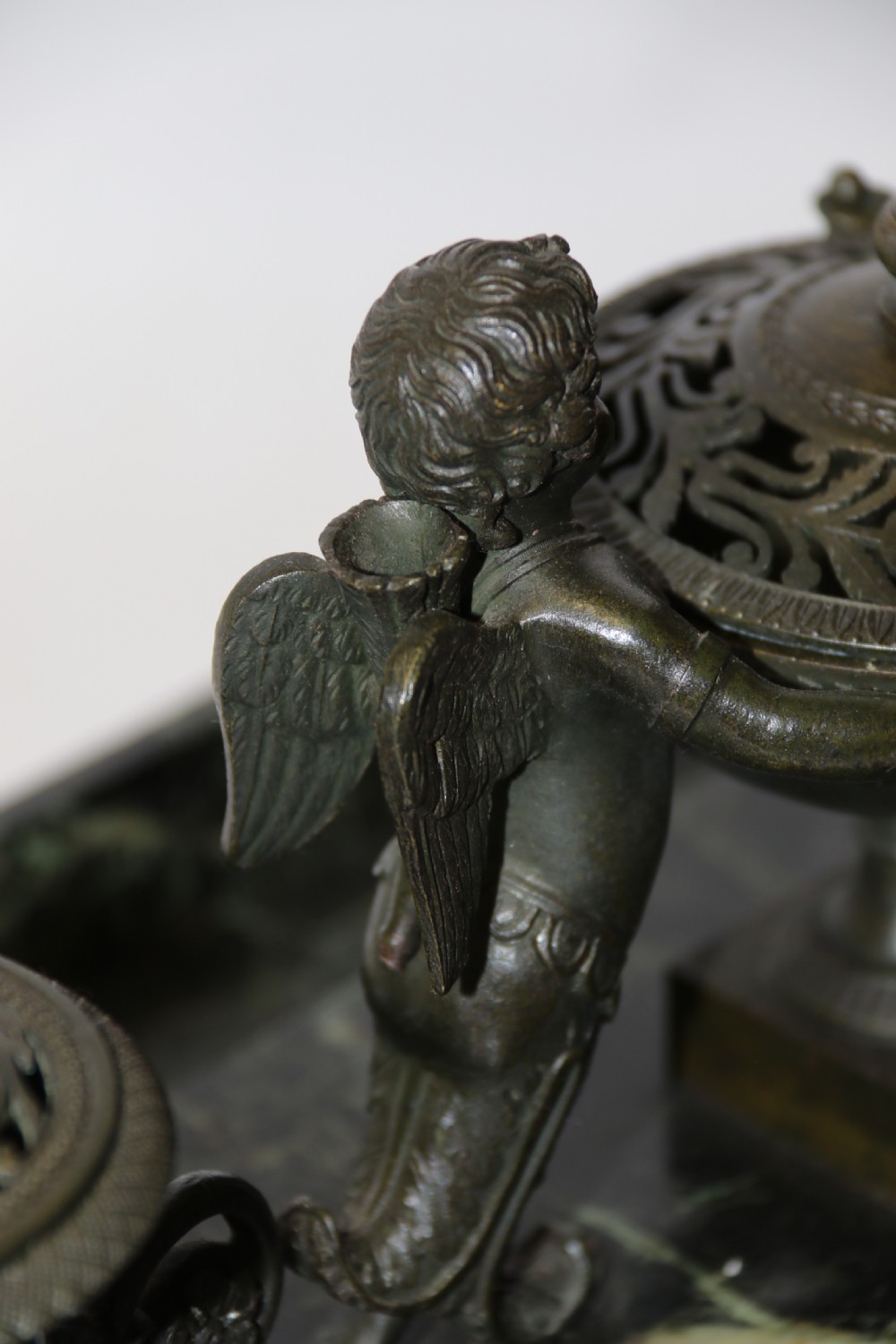 An Empire period dark green marble inkstand featuring dark patinated bronze cherub figures, twin urn inkwells, and carved claw feet. View XXV