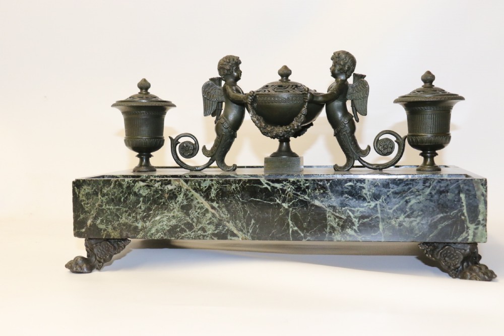 An Empire period dark green marble inkstand featuring dark patinated bronze cherub figures, twin urn inkwells, and carved claw feet. View XXVIII
