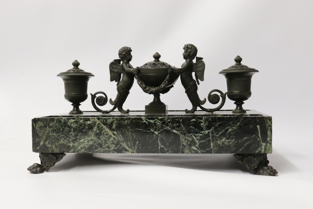 An Empire period dark green marble inkstand featuring dark patinated bronze cherub figures, twin urn inkwells, and carved claw feet. View XXX