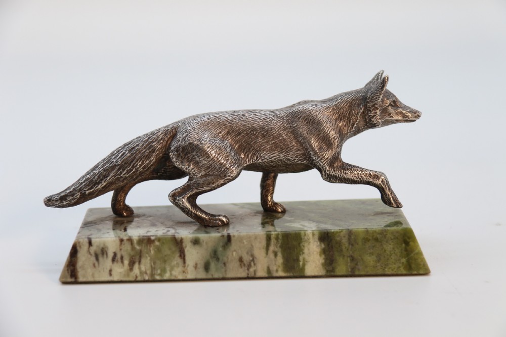 A silvered bronze sculpture depicting a prowling fox mounted on a rectangular green marble plinth.