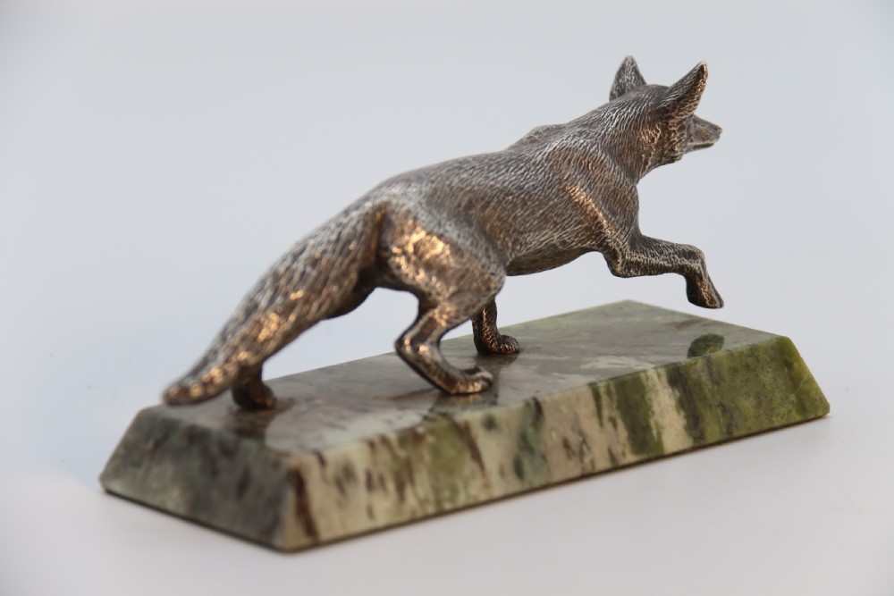 A silvered bronze sculpture depicting a prowling fox mounted on a rectangular green marble plinth. View IV