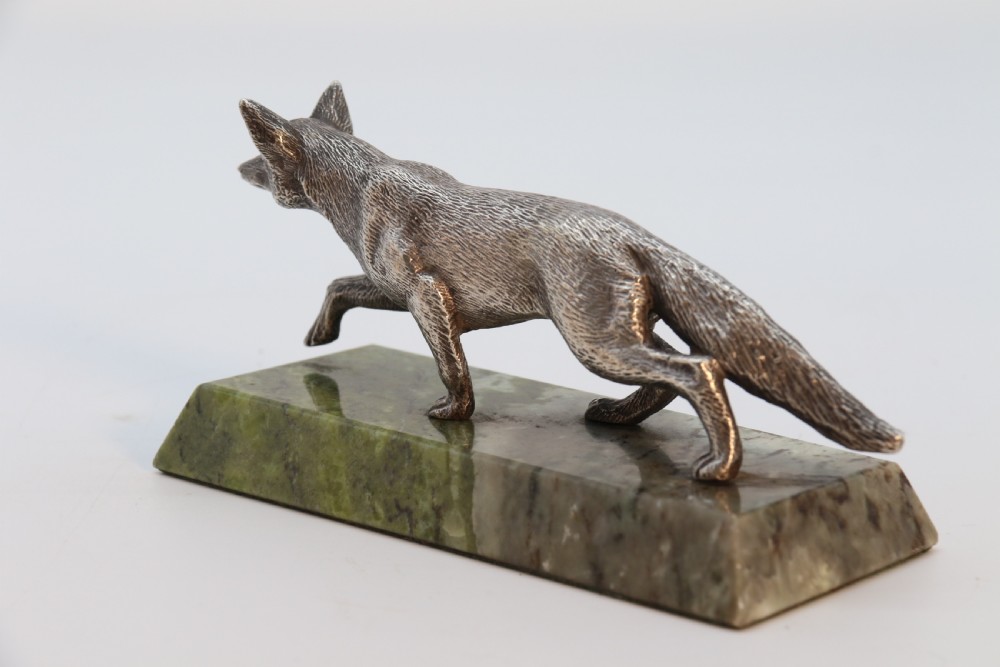 A silvered bronze sculpture depicting a prowling fox mounted on a rectangular green marble plinth. View V