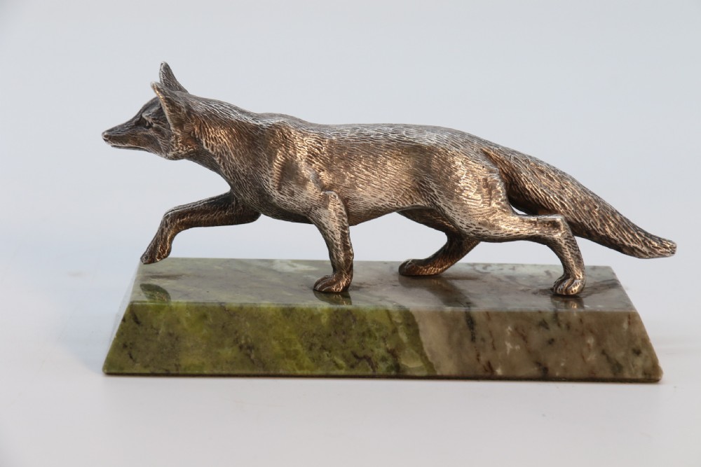 A silvered bronze sculpture depicting a prowling fox mounted on a rectangular green marble plinth. View VI