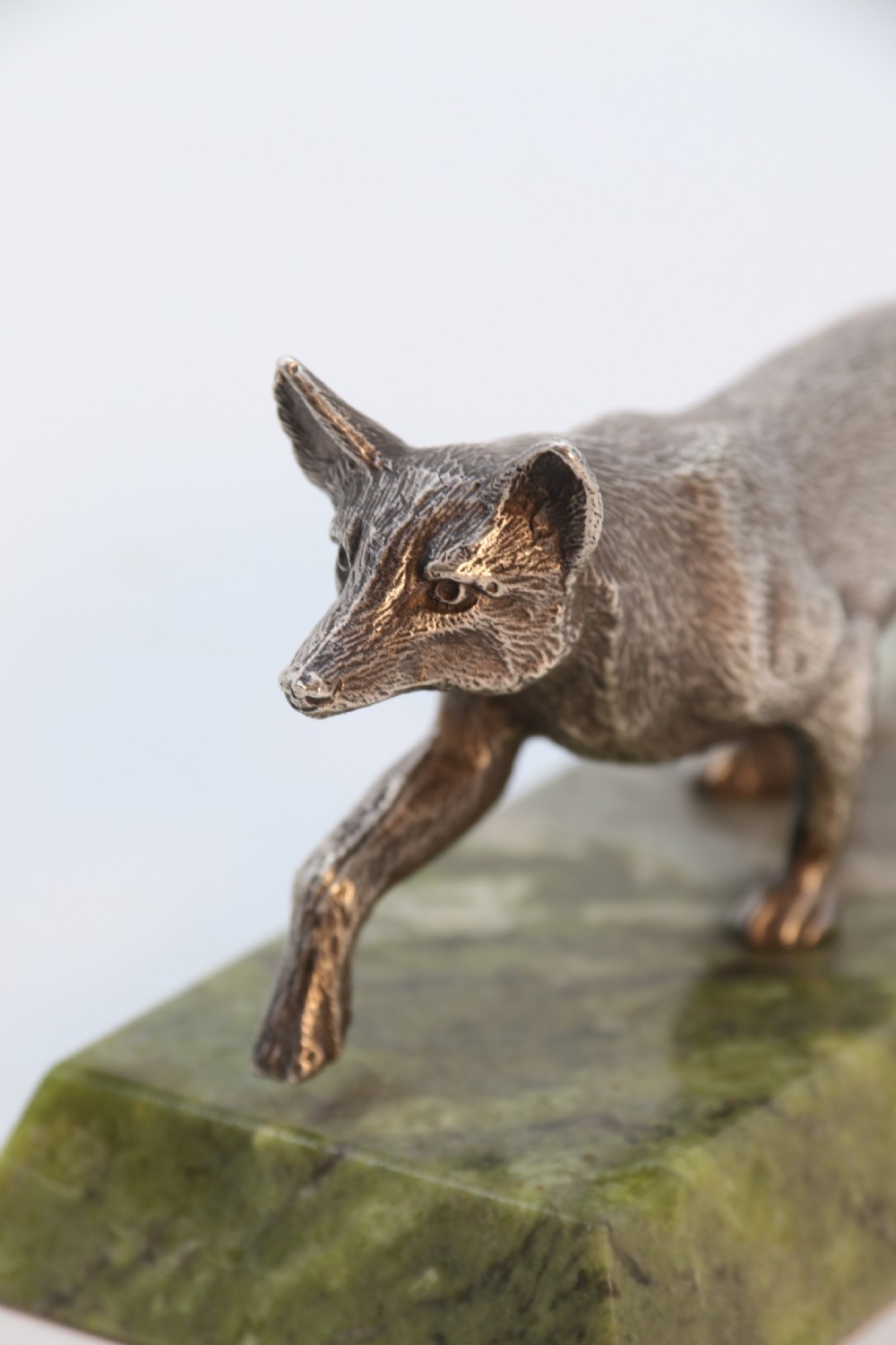 A silvered bronze sculpture depicting a prowling fox mounted on a rectangular green marble plinth. View X