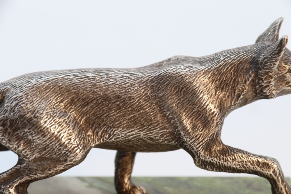 A silvered bronze sculpture depicting a prowling fox mounted on a rectangular green marble plinth. View XII