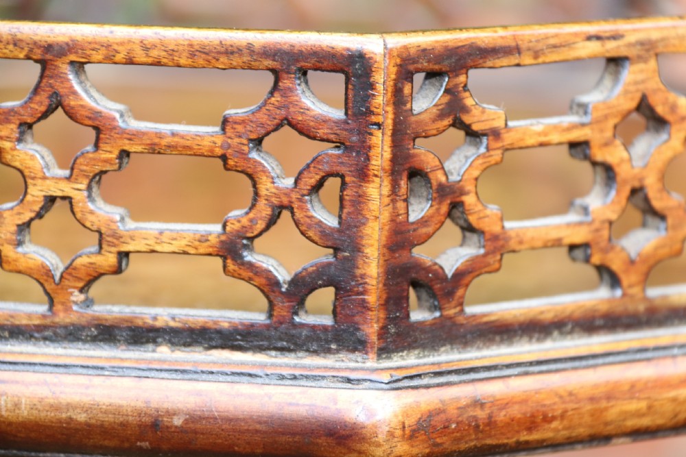 An antique Chippendale mahogany candle stand featuring an octagonal top with a pierced fretwork gallery, a fluted column, and carved tripod legs. View XX