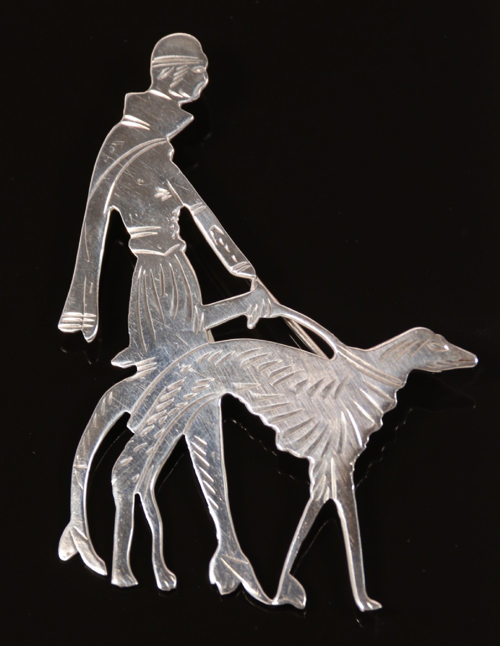 An Art Deco silver brooch  in the form of an elegant 1920s lady walking her borzoi dog.