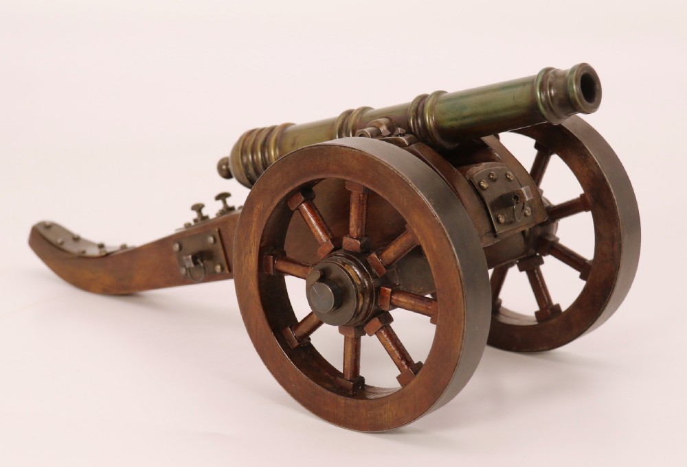 A detailed hand-built scale model of a 17th-century field cannon featuring a patinated brass barrel mounted on a dark timber carriage with spoked wheels.