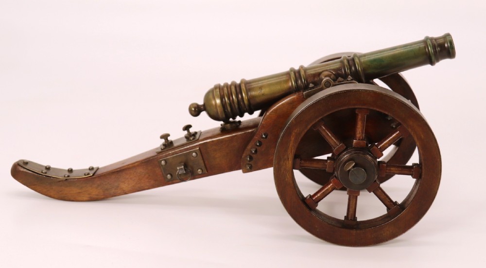 A detailed hand-built scale model of a 17th-century field cannon featuring a patinated brass barrel mounted on a dark timber carriage with spoked wheels. View II