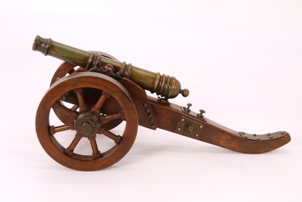 A detailed hand-built scale model of a 17th-century field cannon featuring a patinated brass barrel mounted on a dark timber carriage with spoked wheels. View V
